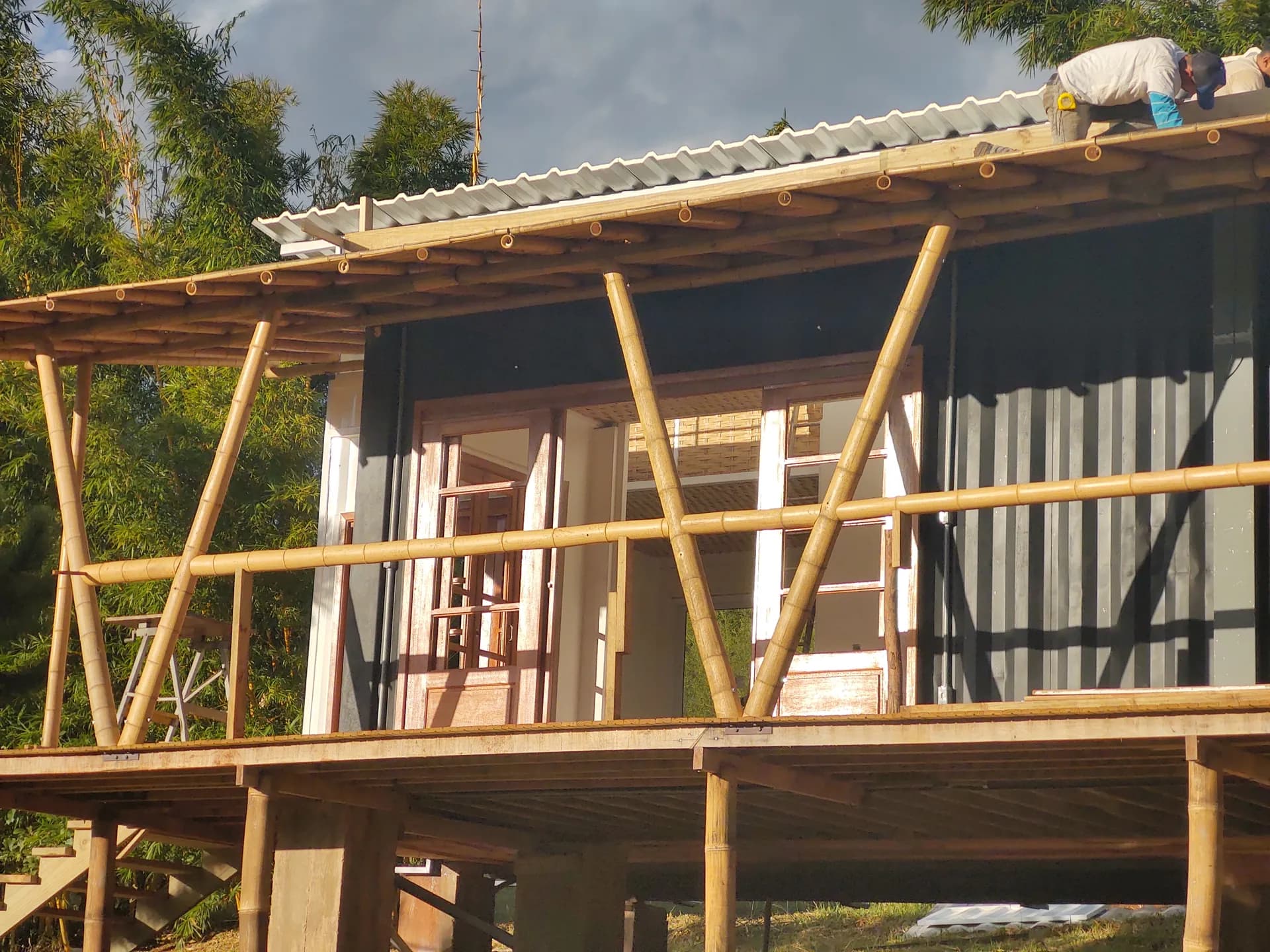 Cobertura metálica concluída e deck com guarda-corpo de bambu, edificação elevada sobre pilotis.