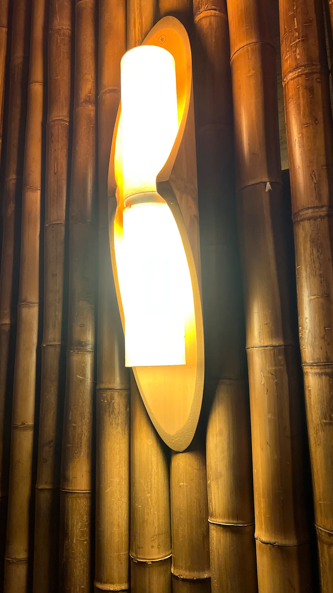 Luminária autoral de bambu sobre parede de colmos, no Vanara Bubble.
