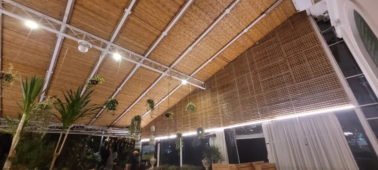 Salão interno do Capim Santo: forro e painéis (muxarabi) de bambu sob estrutura metálica, com iluminação noturna.
