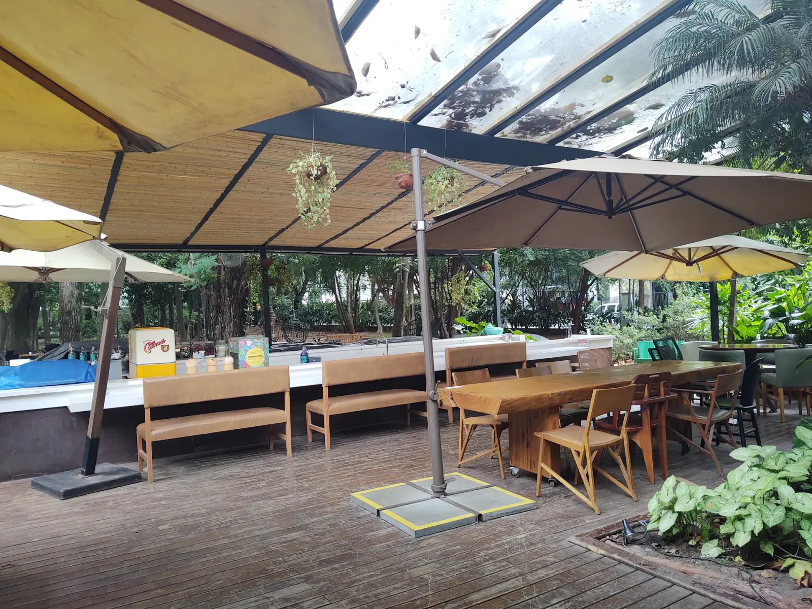 Área externa de refeições no deck do Capim Santo, sob cobertura de bambu e ombrelones, integrada ao jardim.