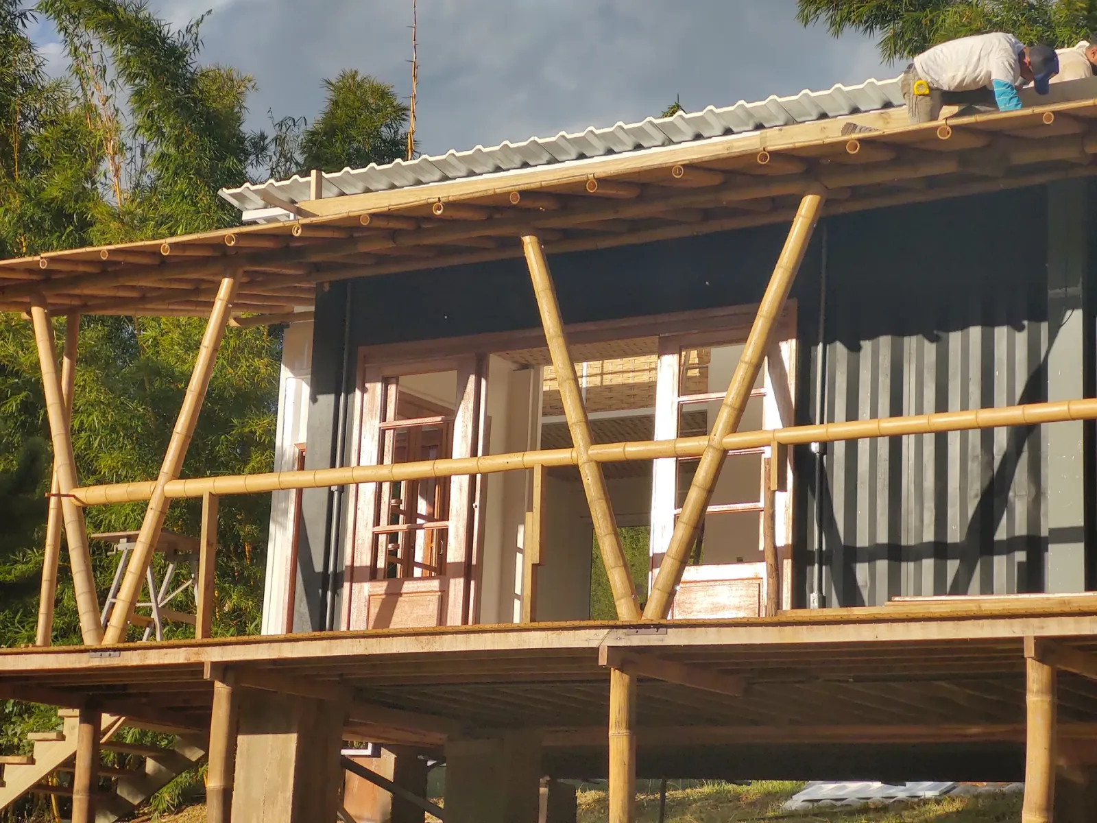 Cobertura metálica concluída e deck com guarda-corpo de bambu, edificação elevada sobre pilotis.