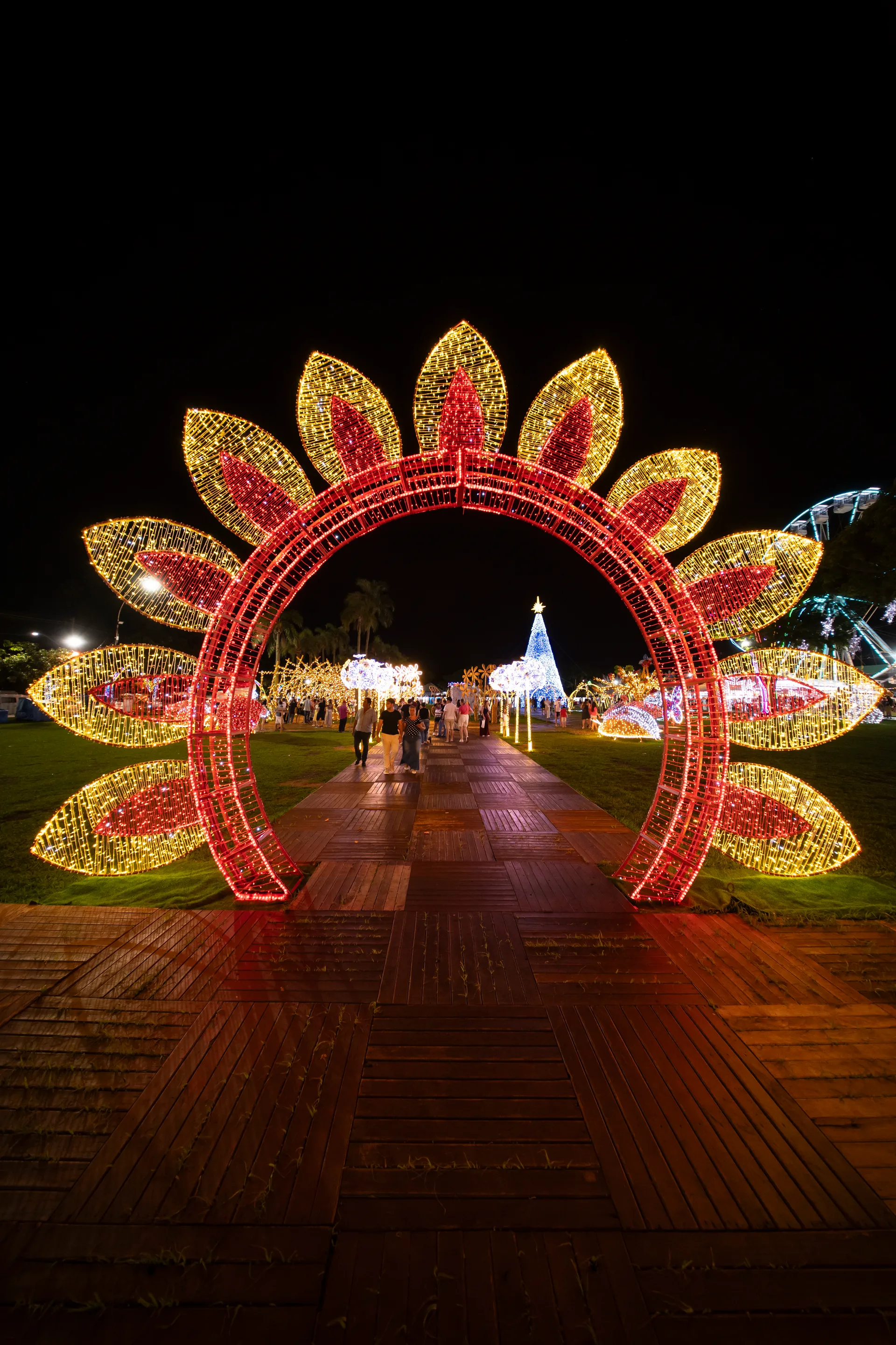 Arco iluminado da Maringá Encantada 2024 sobre o deck do Parque do Japão, com árvore de Natal e roda-gigante ao fundo.